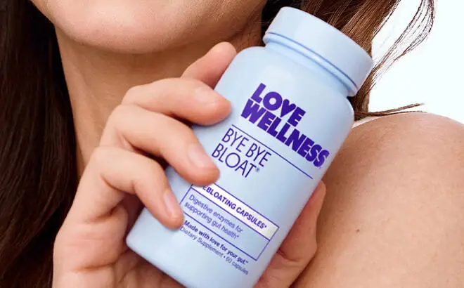 A Hand holding a Bottle of Love Wellness Bye Bye Bloat Supplement Capsules